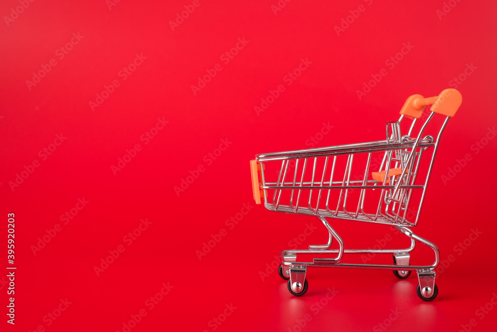 Shopping concept. Side profile close up photo of miniature shopping cart isolated on red background with copyspace