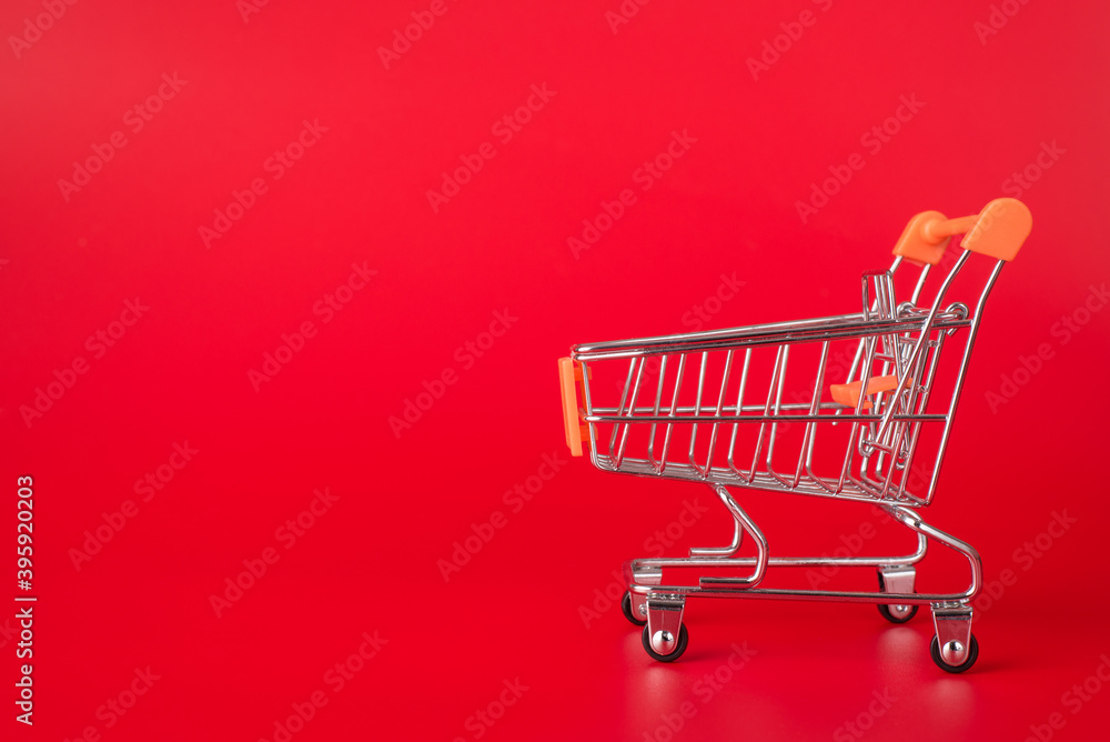Shopping concept. Side profile close up photo of miniature shopping cart isolated on red background with copyspace Shopping concept. Side profile close up photo of miniature shopping cart isolated on red background with copyspace
