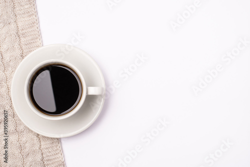 Top above close up view photo of cup of dark fresh hot coffee standing on knitted scarf on white background with empty space