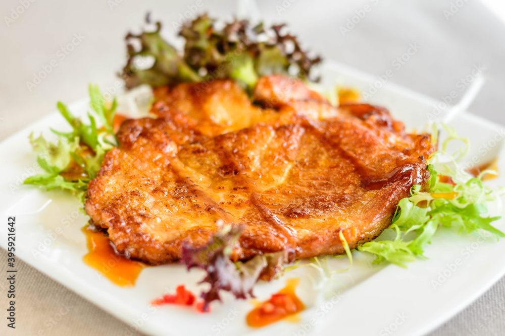 main course of Pan-fried Pork Chop with Soy Sauce served on lettuce on a white plate