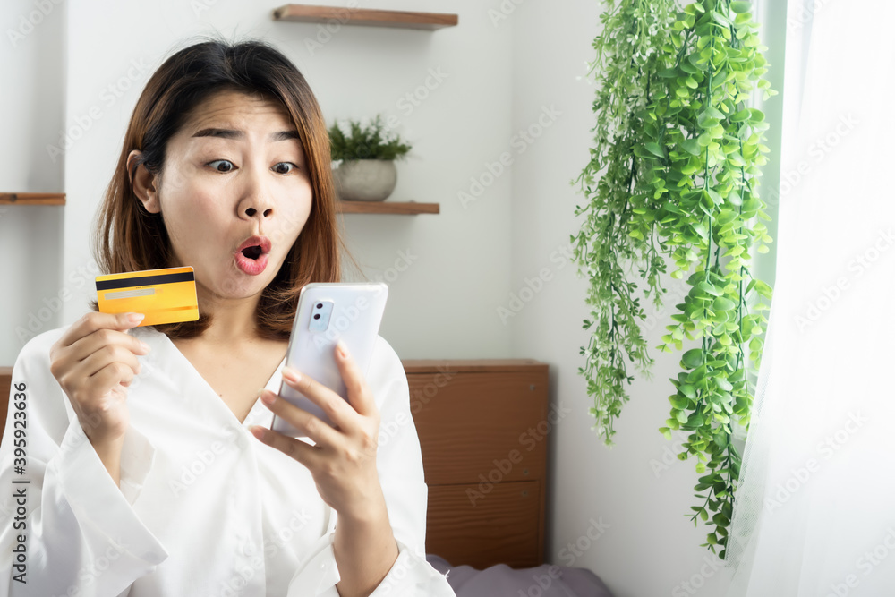 shocked female Asian customer holding credit card shopping online with mobile phone surprised with a promotion shocked female Asian customer holding credit card shopping online with mobile phone surprised with a promotion