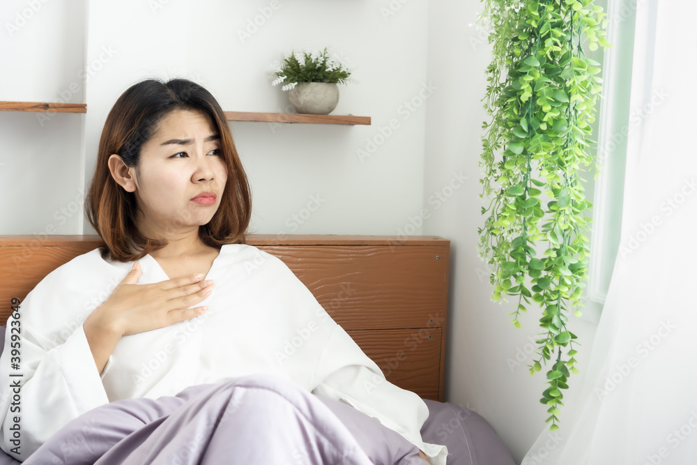 unwell Asian woman suffering from nausea, sore throat ,morning sick sitting in bed unwell Asian woman suffering from nausea, sore throat ,morning sick sitting in bed