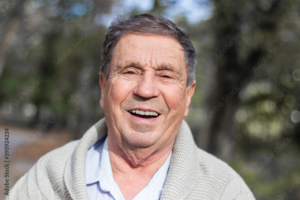 Portrait of happy senior man smiling, in the public park, outdoors. Old man relaxing outdoors and looking at camera. Portrait of elderly man enjoying retirement Portrait of happy senior man smiling, in the public park, outdoors. Old man relaxing outdoors and looking at camera. Portrait of elderly man enjoying retirement