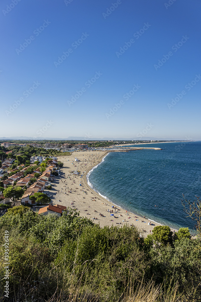 Sandy Mediterranean beach Le Racou in Argeles sur Mer with its old fishermens houses and the harbor in background, Roussillon, Pyrenees Orientales, France.