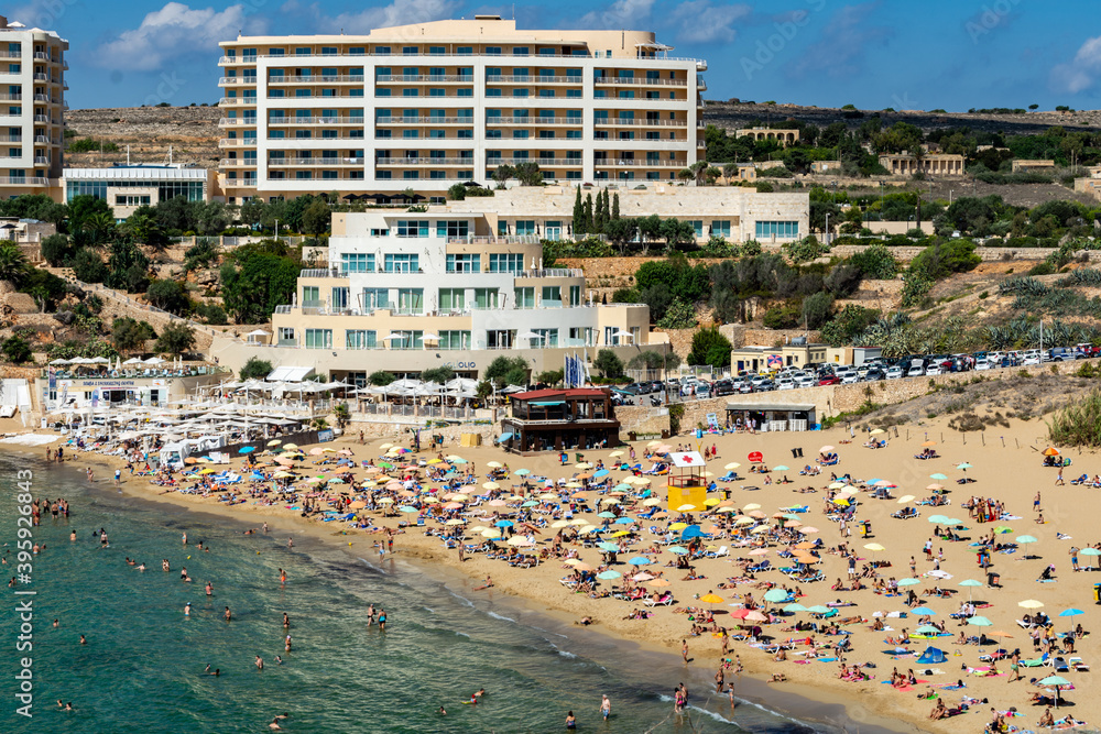 Sunbather on Golden Bay Beach overlooked by hotels in mellieha, Malta.