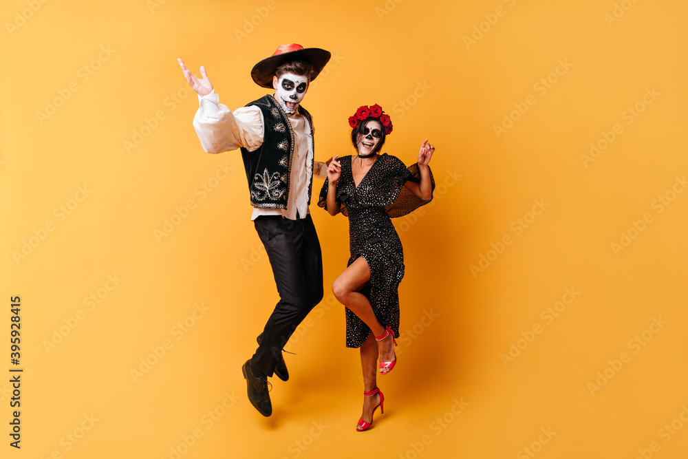 Obraz premium Portrait in full growth of dancing funny men and his sweet lady. Girl with crown of roses and painted face is enjoying Halloween with her boyfriend