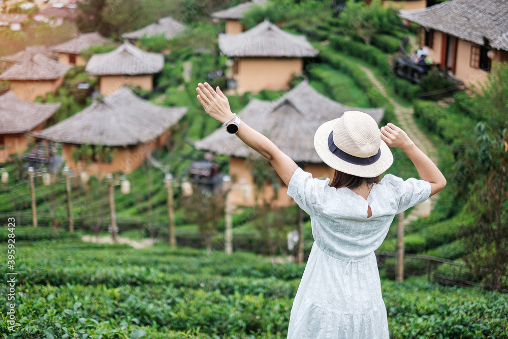 Fototapeta premium Happy tourist woman in white dress enjoy beautiful Tea garden.Traveler visiting in Ban Rak Thai village, Mae Hong Son, Thailand. travel, vacation and holiday concept