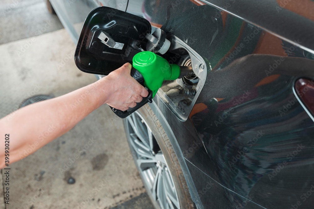 Woman pours fuel into the tank of a black car on gasoline station. Transportation concept. Beautiful backgrounds.