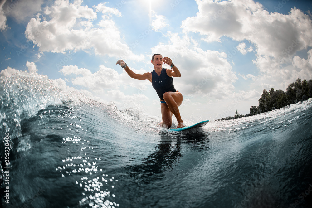beautiful wet woman rides wave on surf board against the blue sky