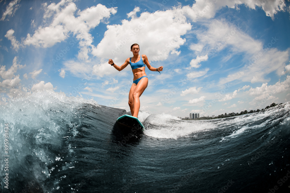 Active young woman in blue swimsuit having fun on the board on the river