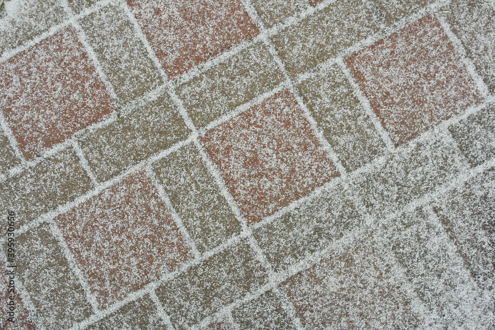 Fototapeta premium The first snow on the tile-paving stones, the material is an abstract background.