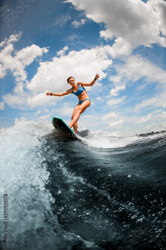 Sexy woman having fun on the board on the river wave against blue sky