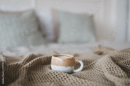 Cup of coffee with warm plaid. Breakfast in bed. White stylish cozy bedroom. Hygge concept. Copy space. Flat lay, top view.