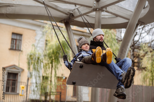 father with cute 6 year old son swinging on large bench swings. brothers with dad walking on playground