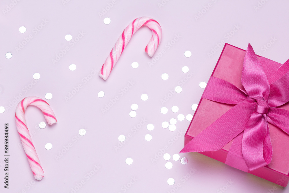 Pink gift with candy cane and silver confetti. Copy space for advertising. Concept to celebrate and to congratulate.