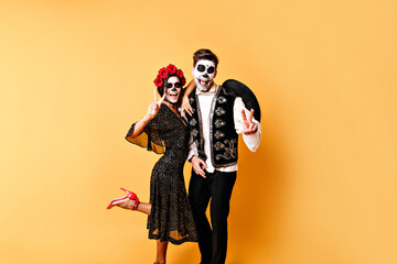 Funny shot of full-length couple of lovers in halloween costumes having fun against backdrop of orange wall.