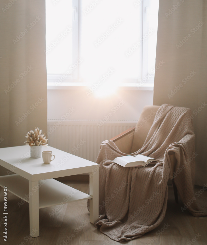 Cozy interior with coffee table, armchair and plaid near window. Sunny living room. Scandinavian interior. Slow living concept Cozy interior with coffee table, armchair and plaid near window. Sunny living room. Scandinavian interior. Slow living concept