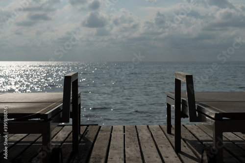 Two metal sunbeds lay on the wooden floor and have a sea background against the evening light.