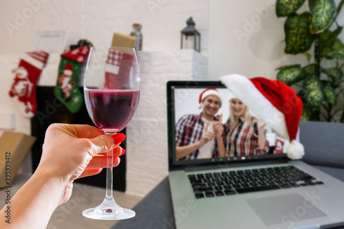 Happy woman making a toast on video call celebrating christmas with glass of wine online during coronavirus outbreak - Focus on wine glass