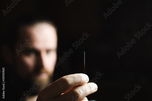 A man looks at an acupuncture needle catching the light