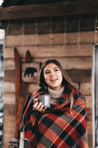 Young caucasian happy woman in a plaid is drinking a hot drink on the backyard, enjoying Christmas morning.