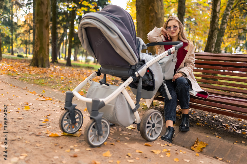 Mother with stroller while walking in the park sat down on bench to rest Mother with stroller while walking in the park sat down on bench to rest