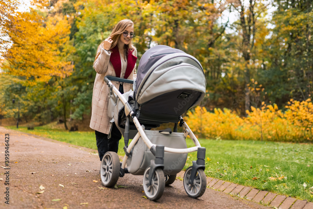 Cheerful mother with stroller walks in autumn park away from the bustle of the city Cheerful mother with stroller walks in autumn park away from the bustle of the city