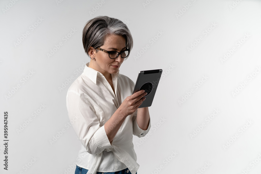 Senior grey haired woman in white shirt using digital tablet. The use of technology by the elderly browsing internet shopping online on pad isolated on white background. Senior grey haired woman in white shirt using digital tablet. The use of technology by the elderly browsing internet shopping online on pad isolated on white background.