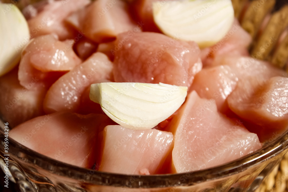 Raw chicken meat in a plate, cut into pieces, on top are pieces of onions.
