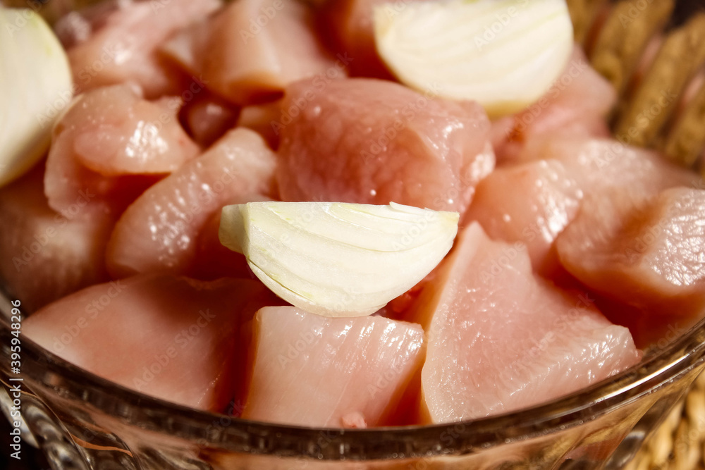 Raw chicken meat in a plate, cut into pieces, on top are pieces of onions. Raw chicken meat in a plate, cut into pieces, on top are pieces of onions.