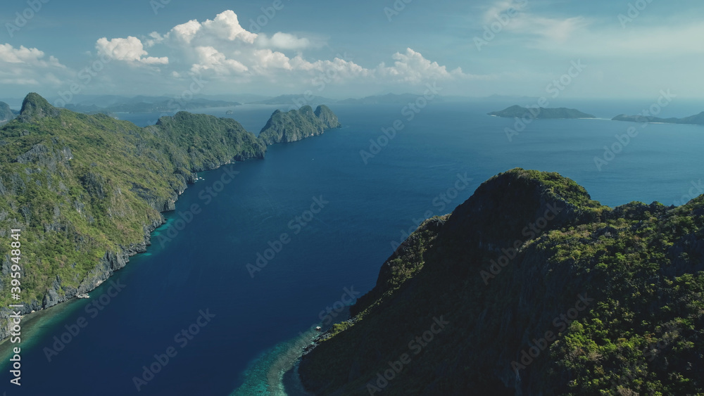Aerial view of mountain greenery island at ocean bay on summer sunny day. Green forest highland isle on blue water of tropical Philippines. Cinematic seascape at soft light drone shot