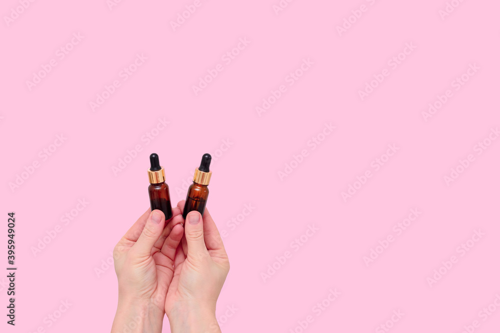 Cosmetic serum in transparent glass dropper bottles on a pink background in a woman's hand. the concept of natural skin care products. Essence skin care products for beautiful healthy skin Cosmetic serum in transparent glass dropper bottles on a pink background in a woman's hand. the concept of natural skin care products. Essence skin care products for beautiful healthy skin