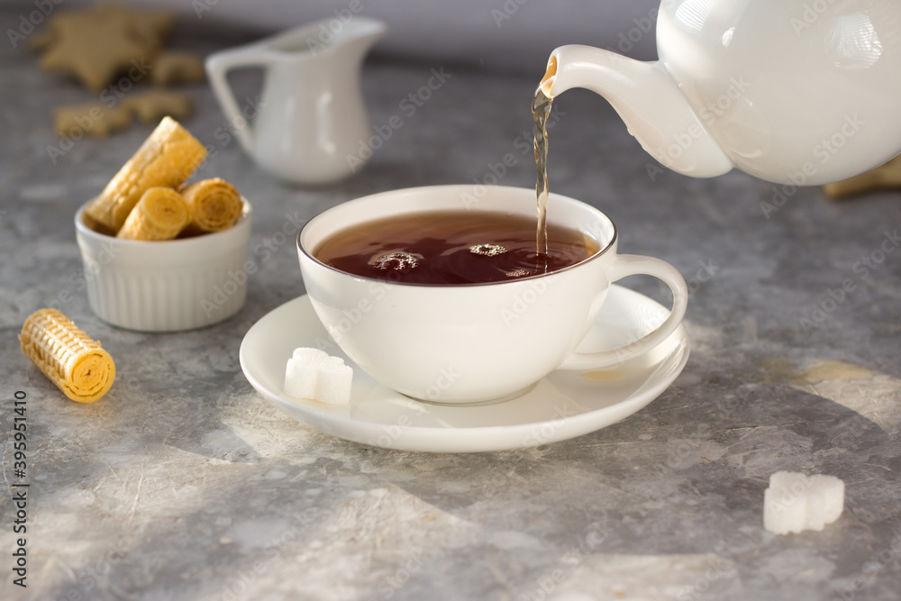 Tea from the teapot is poured into a white mug. A stream of tea pours into the Cup with a splash Tea from the teapot is poured into a white mug. A stream of tea pours into the Cup with a splash
