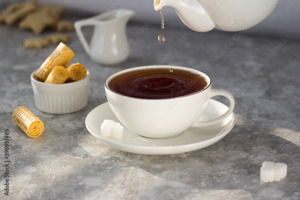 Tea from the teapot is poured into a white mug. A stream of tea pours into the Cup with a splash Tea from the teapot is poured into a white mug. A stream of tea pours into the Cup with a splash