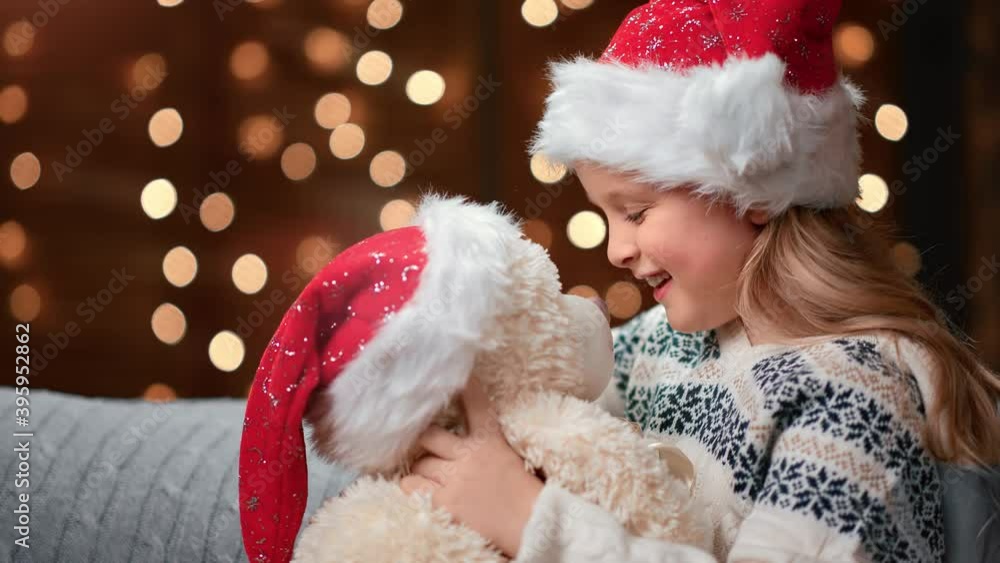 Happy girl in Santa Claus hat smiling hugging teddy bear. Medium close up shot on 4k RED camera