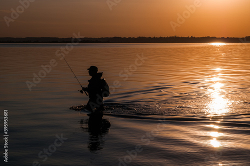 Angler with fishing rod in hand walking in water during sunset in Rewa - Poland.