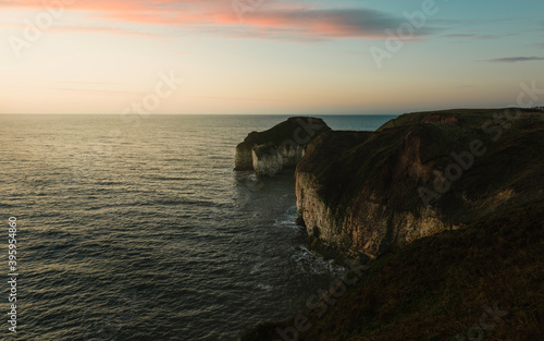 Sunrise over sea and eroded chalk cliffs under bright sky along coastline. Flamborough, UK.