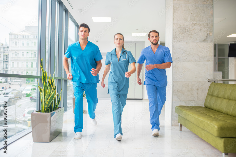 Fototapeta premium Three doctors running throtugh the hospital corridor being in a hurry