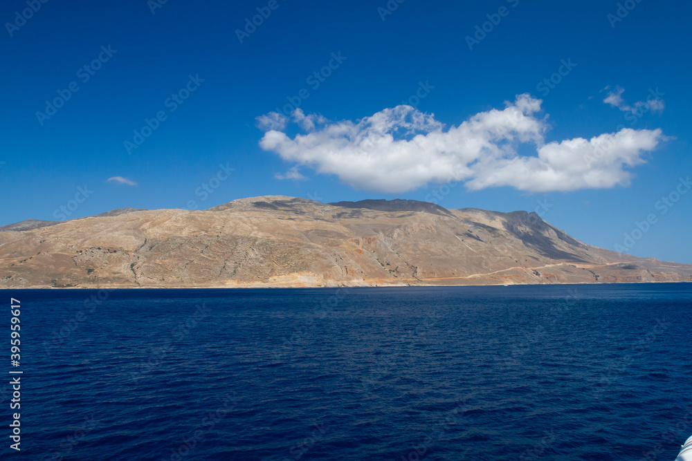 sea and the waves break on the rock and in the background is a mountain and clouds and a blue sky during the day