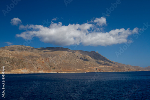 sea and the waves break on the rock and in the background is a mountain and clouds and a blue sky during the day