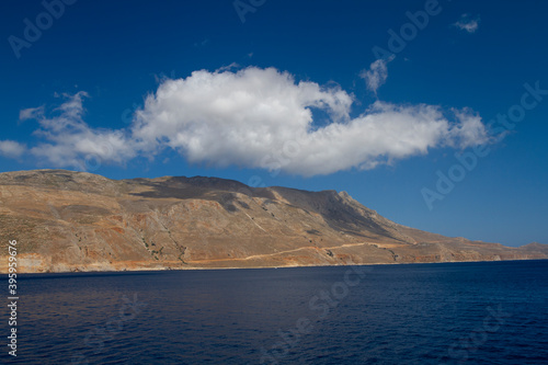 sea and the waves break on the rock and in the background is a mountain and clouds and a blue sky during the day