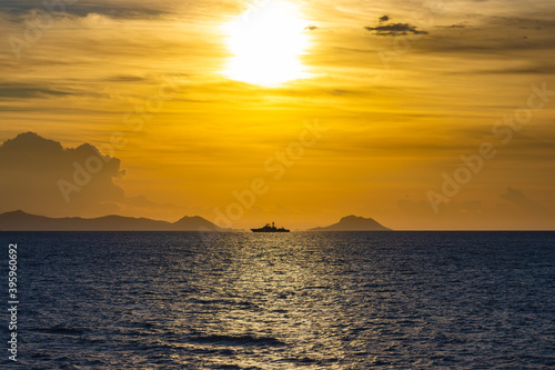 Schiff am Horizont zwischen Insel und Festland vor der aufgehenden Sonne