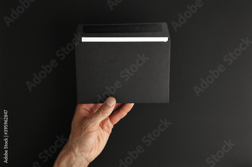 male hand holding blank black envelope with white letter on black background, mockup, copy space