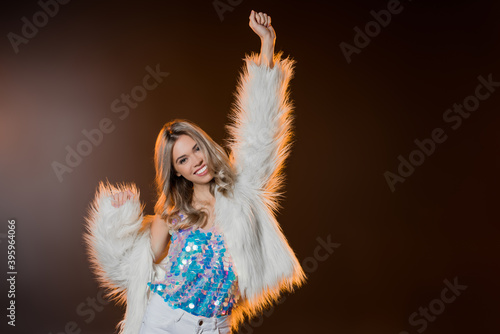 blonde woman in faux fur jacket standing with outstretched hand on black