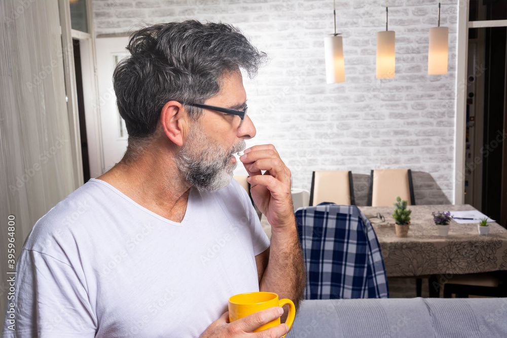 Photo of Sick mature man holding pill and glass of water at home. Serious man ready to take a pill Photo of Sick mature man holding pill and glass of water at home. Serious man ready to take a pill