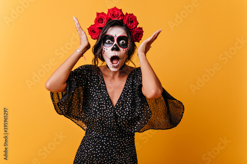 Girl from Latin America with skull makeup reacts emotionally and poses for portrait in orange studio