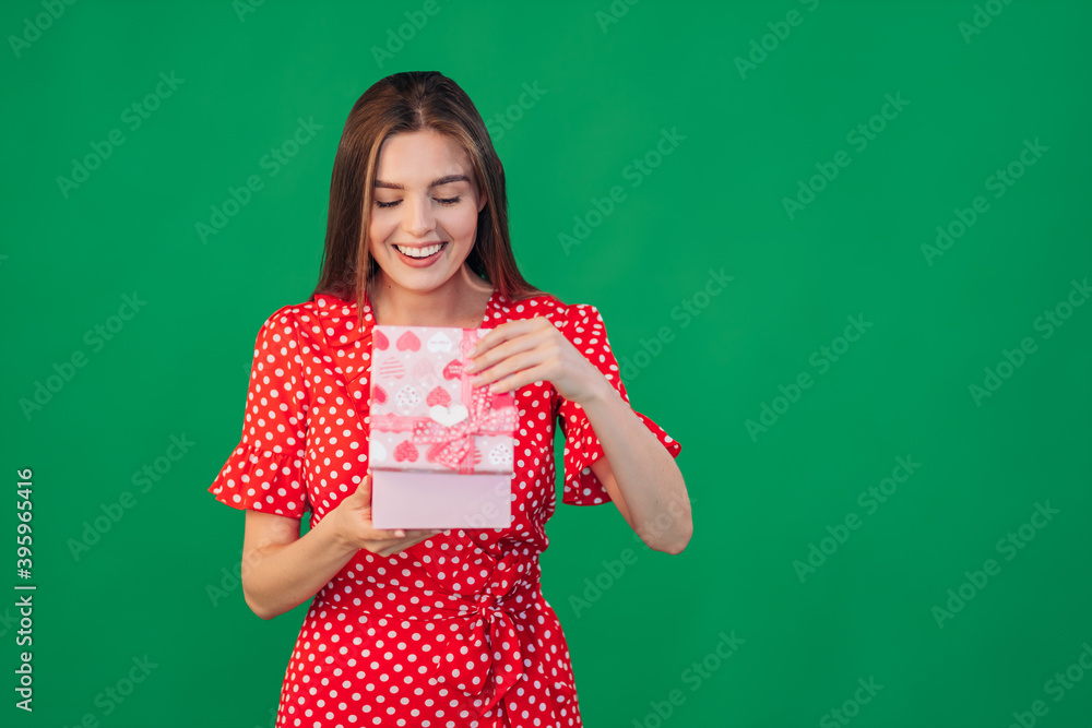 A portrait of a funny, surprised, curious girl in a dress who looks into a gift box, unfolds the gift and looks inside with interest, opening her mouth in amazement. A portrait of a funny, surprised, curious girl in a dress who looks into a gift box, unfolds the gift and looks inside with interest, opening her mouth in amazement.