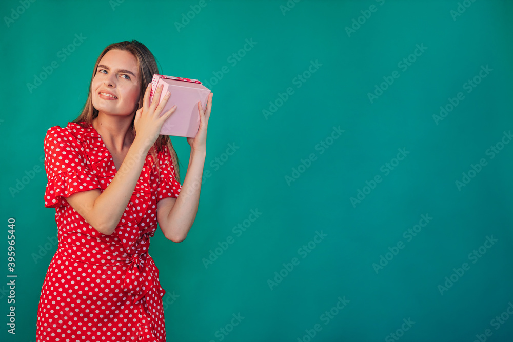 Guess what's inside. Excited girl shaking present and listening to rattling in gift box isolated on turquoise studio wall. Guess what's inside. Excited girl shaking present and listening to rattling in gift box isolated on turquoise studio wall.