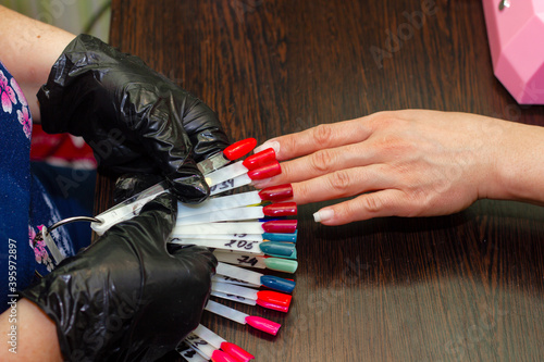 girl chooses color of nail polish for manicure in beauty salon using plastic samples
