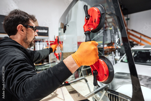 Automobile technician worker replacing windscreen or windshield of a car in auto service station garage. High quality photo